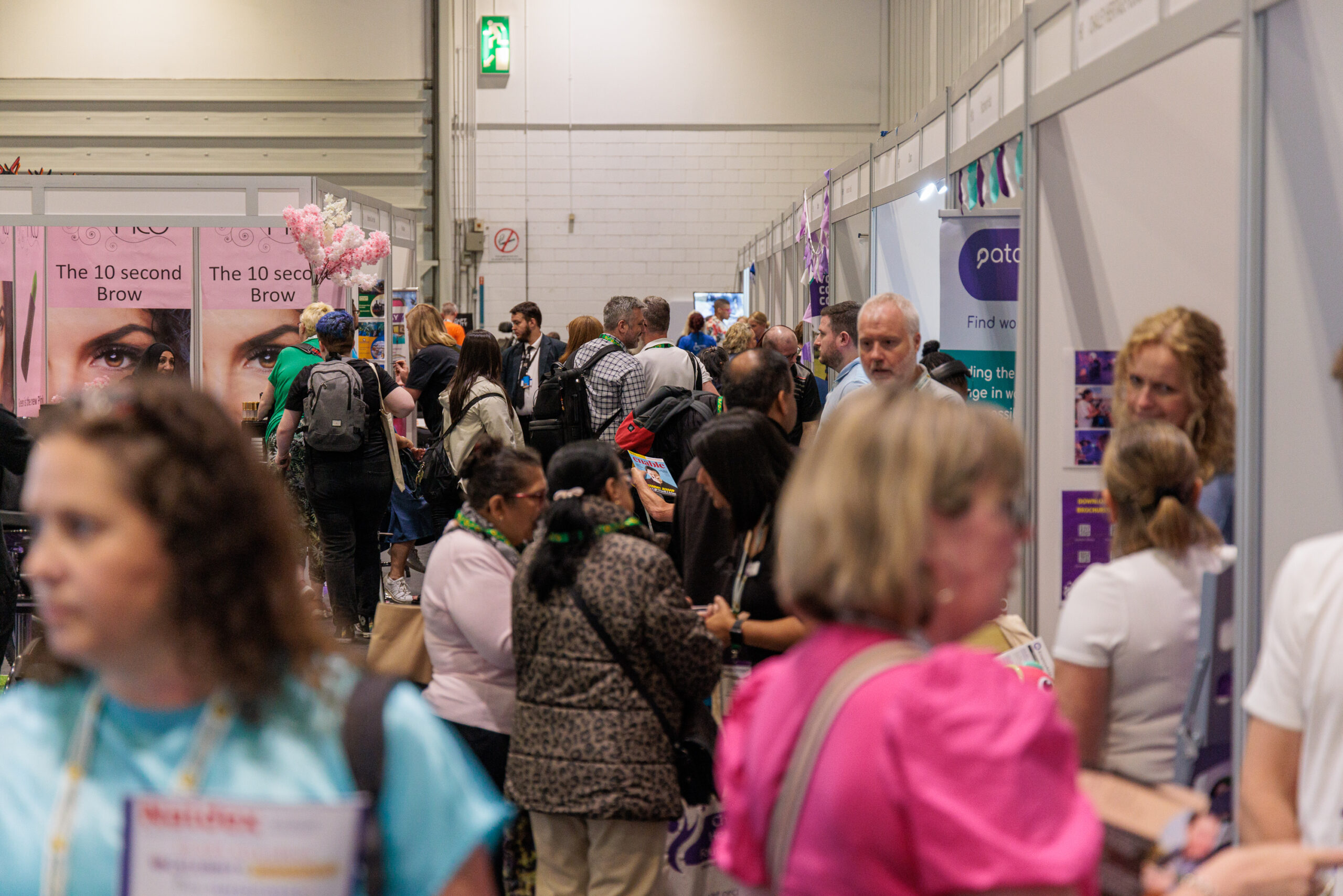 A view looking down a busy aisle of the Disability Expo 2023 exhibition hall, featuring delegates chatting to exhibitors at their stands.