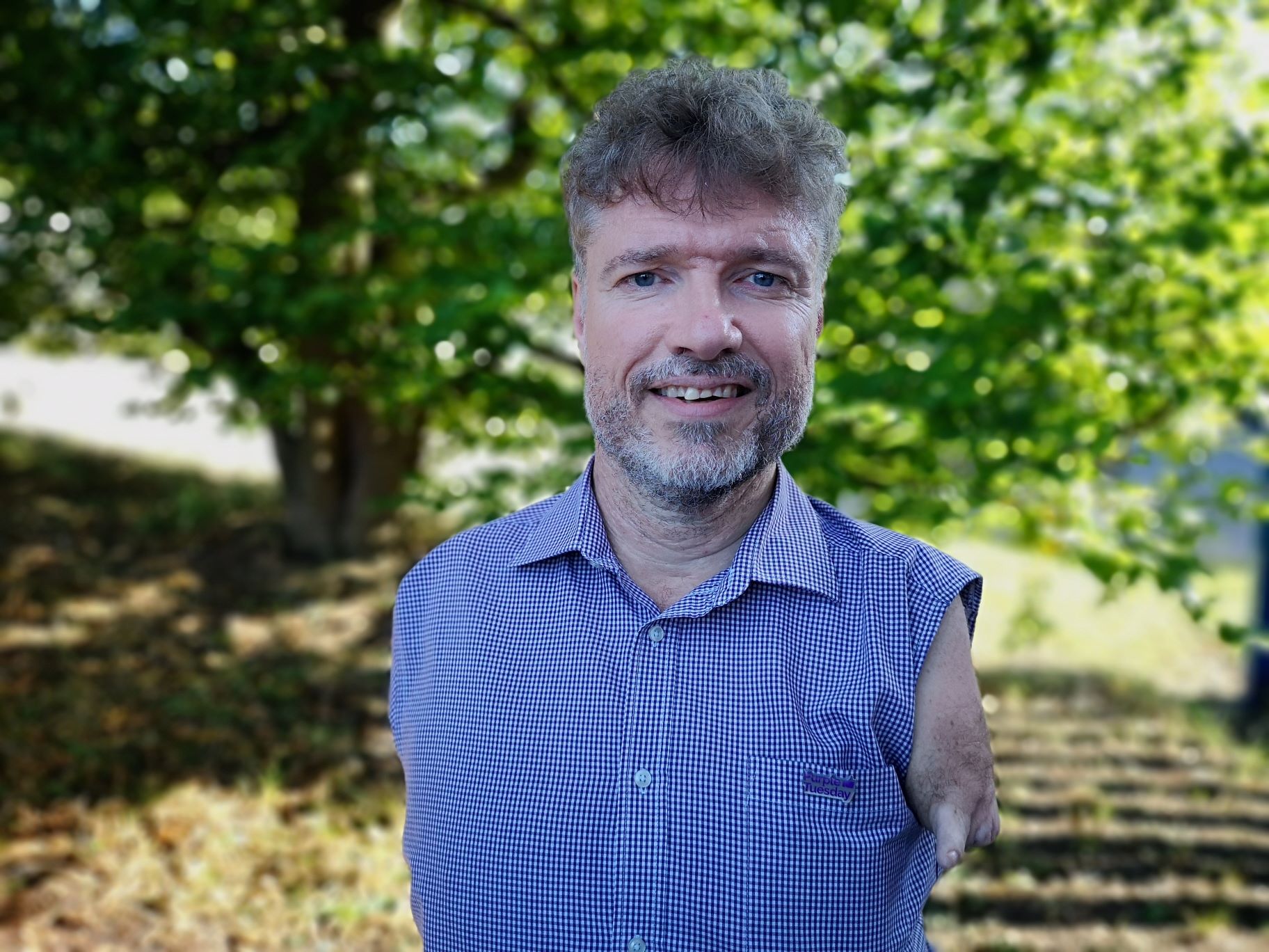 Image of Mike Adam, wearin a blue shirt, curly hair, some facial hair and smiling